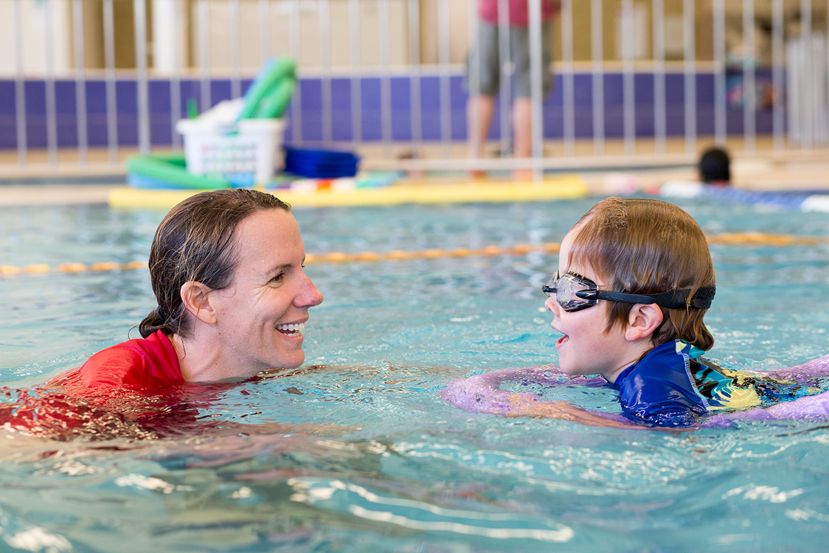 Swim instructor in the water teaching a young boy to swim