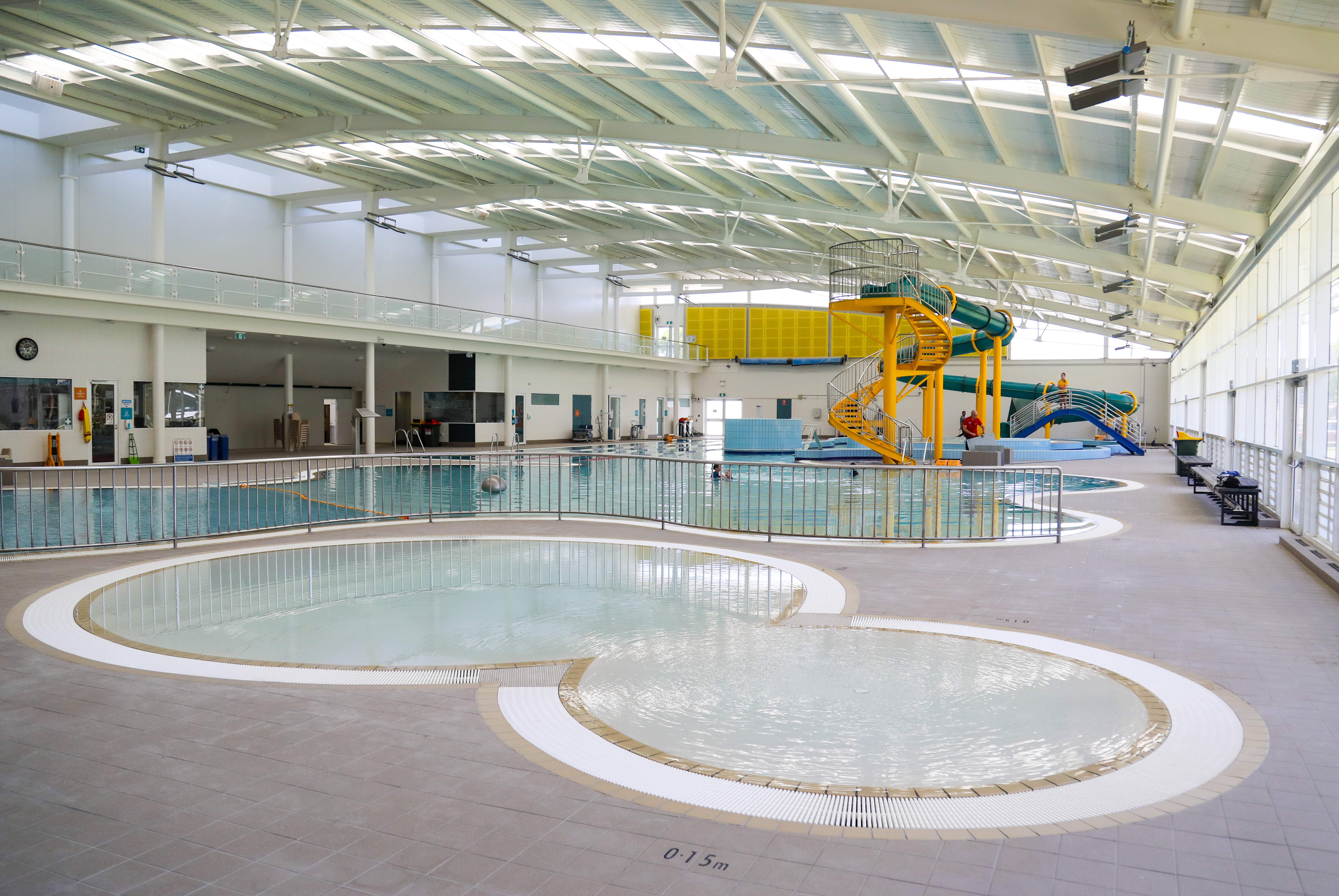 A photo of a small kids pool with the main indoor pool in the background