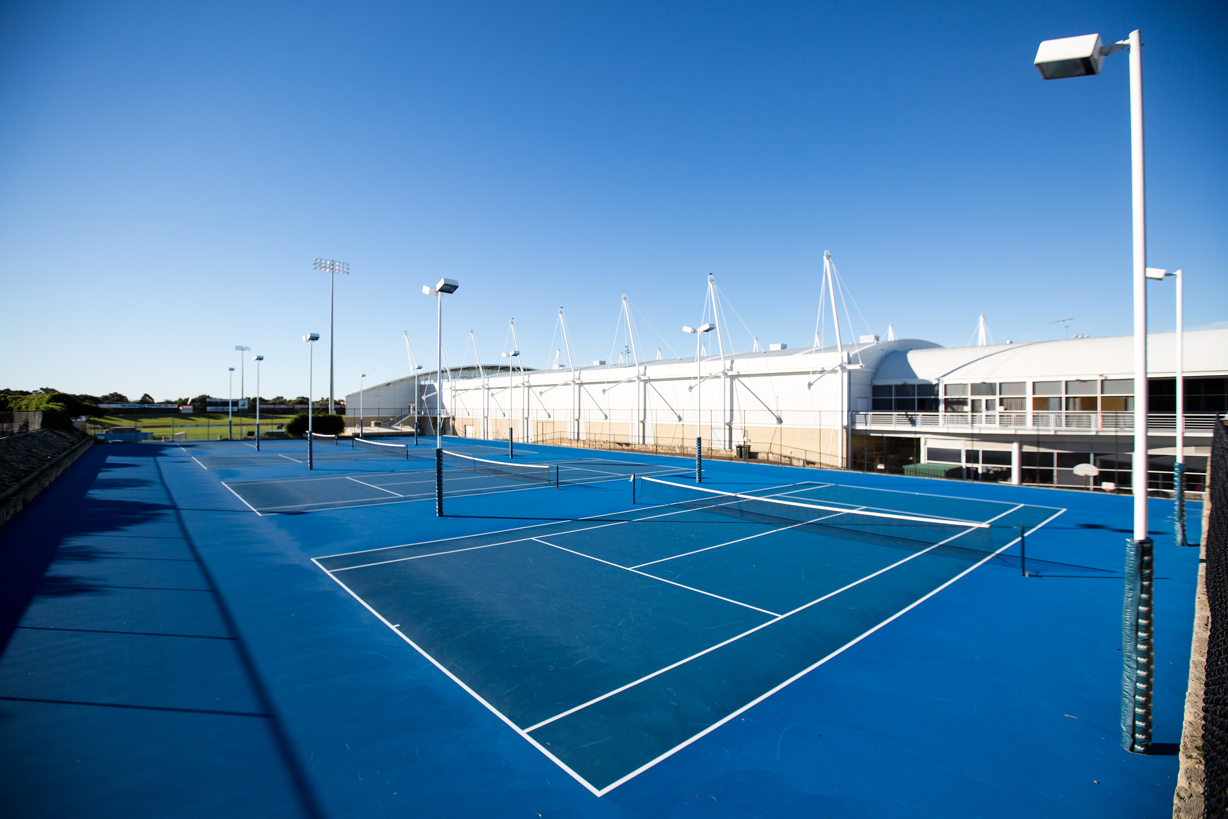 A photo of three side by side astroturfed tennis courts at Arena Joondalup