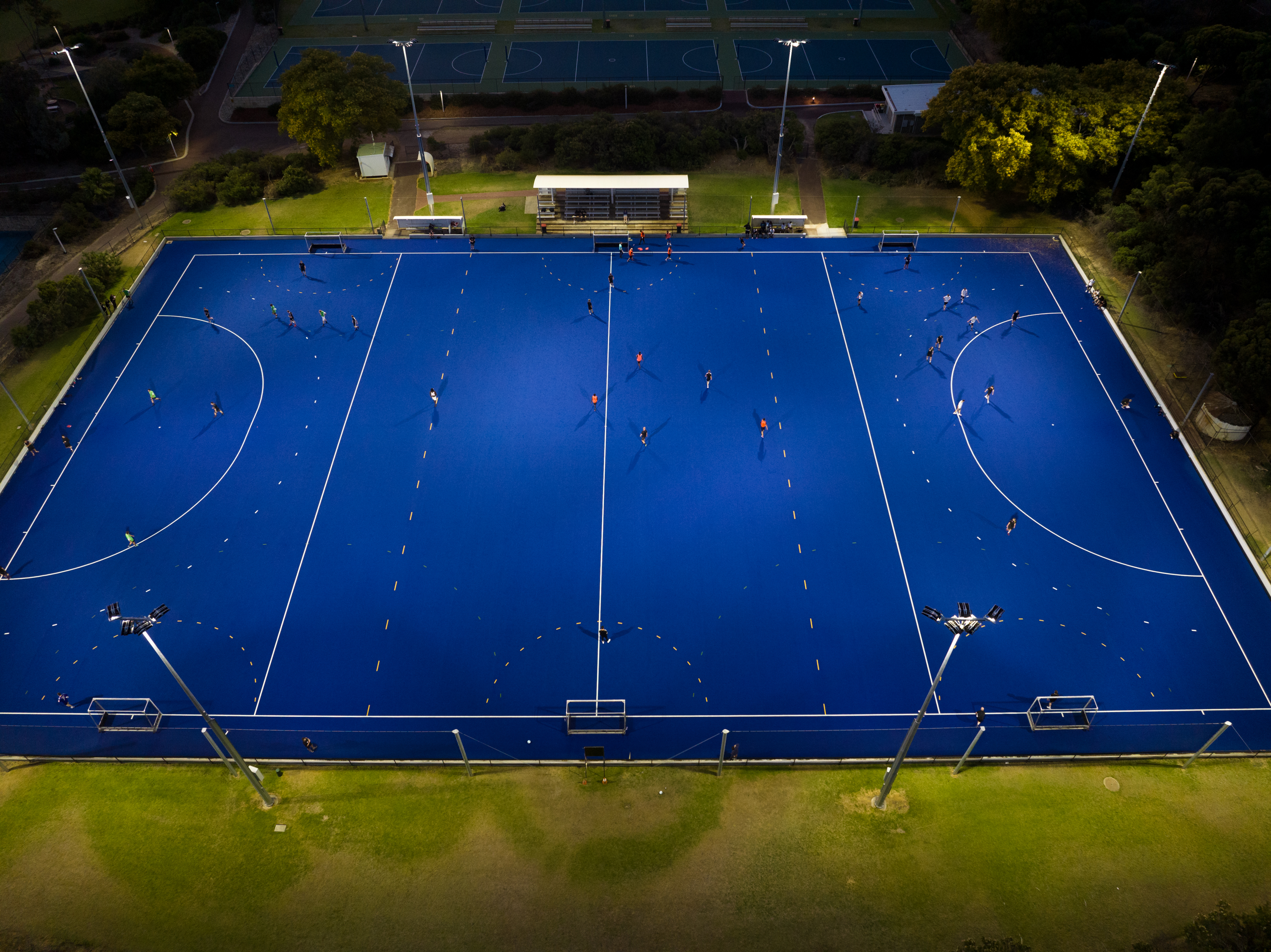A top down photo of a hockey game being played on a blue astroturf court at Arena Joondalup